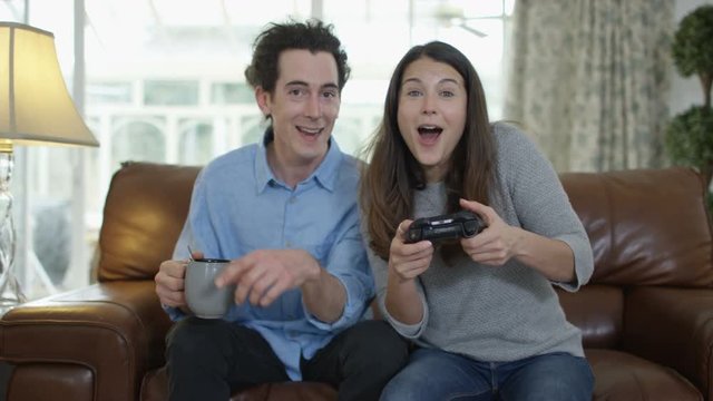  Competitive woman playing video games at home, with boyfriend beside her.