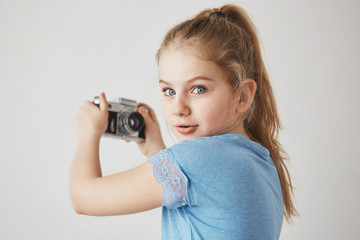 Close up portrait of cheerful cute girl with blonde hair and blue eyes, looking in camera with interested expression, going to take a selfie.