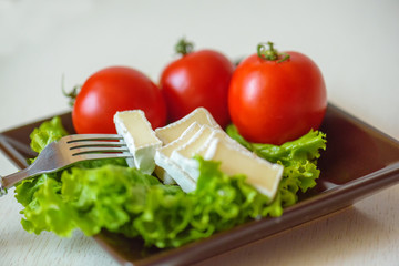 Tomatoes and cheese slices lie on a sheet of fresh salad in a plate.