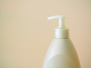 Top part of white lotion cream pushing bottle, with pale pink yellow painted grainy texture cement wall background