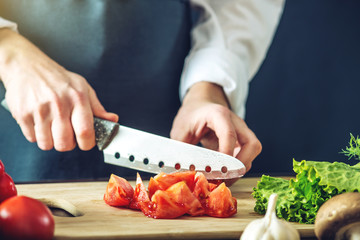 The chef in black apron cuts vegetables. Concept of eco-friendly products for cooking