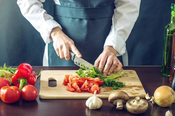 The chef in black apron cuts vegetables. Concept of eco-friendly products for cooking