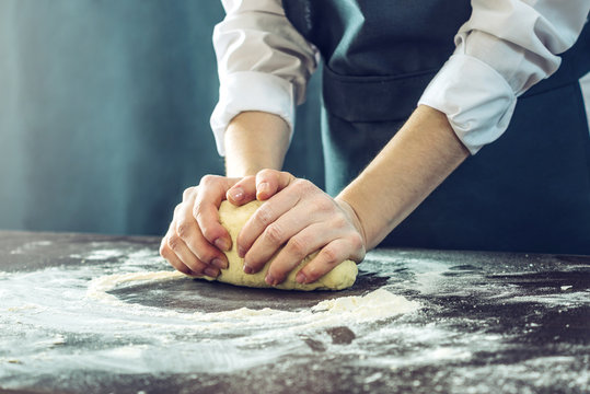 The chef in black apron makes pizza dough with your hands on the table