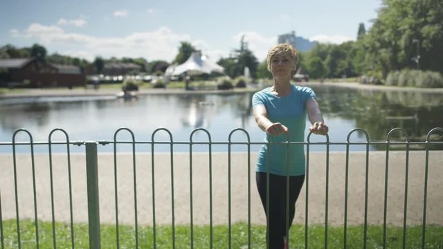  Healthy & active mature lady running in the park stops to do some stretches
