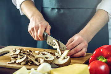 De chef-kok in zwarte schort snijdt champignons met een mes. Concept van milieuvriendelijke producten om te koken
