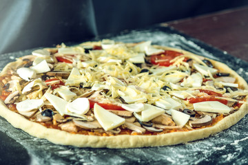 Homemade large vegetarian pizza with ingredients ready to bake on a dark table