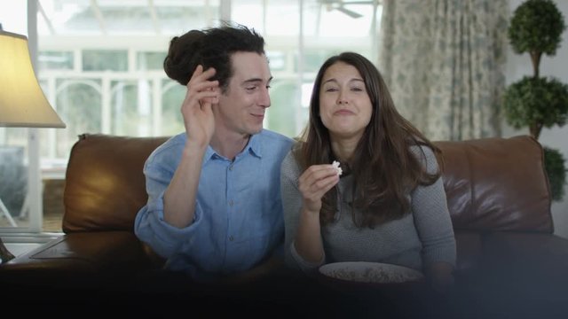  Couple watching TV & eating popcorn, laughing at the action on screen