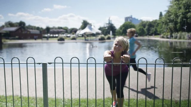  Healthy & active mature lady running in the park stops to do some stretches
