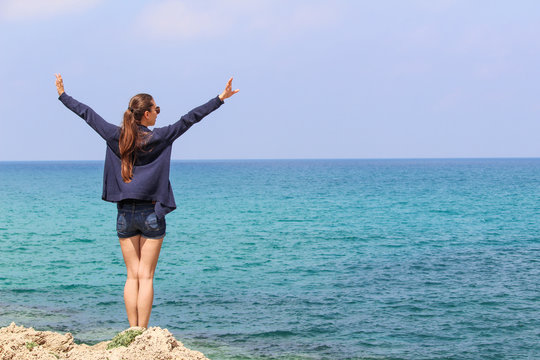 A woman with her arms up in front of the sea