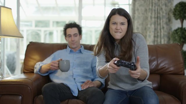  Competitive woman playing video games at home with bored boyfriend beside her