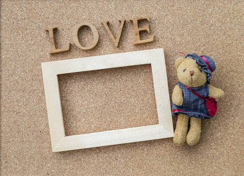 Love text and wooden frame with little cute bear on corckboard background