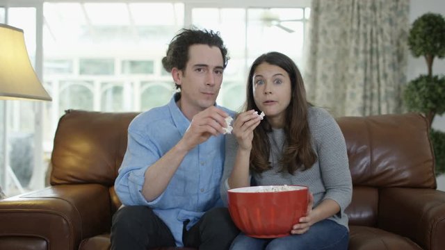  Couple watching TV & eating popcorn, shocked reaction the action on screen