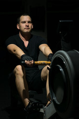 Fototapeta premium training on a cardio boating machine. against a dark background