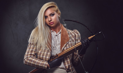 Studio portrait of blond old fashioned female holds a crossbow.