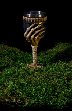 Halloween goblet decorated with skeleton hand and skulls on forest moss.