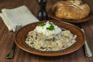 Fricassee of chicken with mushrooms with rice in a ceramic bowl on brown wooden table. 