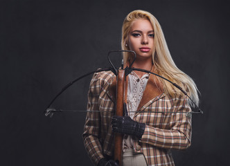 Studio portrait of blond old fashioned female holds a crossbow.