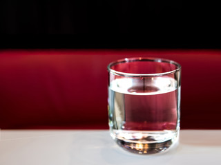 A soft focused image of a glass of water on white table with the red and black background
