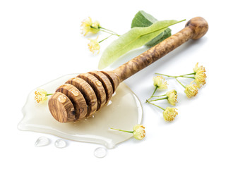 Wooden dipper lays in honey puddle and linden flowers.