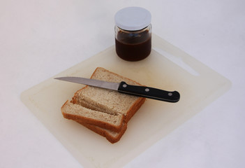 The knife on the cutting bread with jam on the chopping board, white background. Preparation of simple breakfast on the morning.
