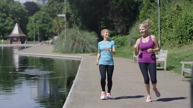  Healthy mature female friends stop to take a break from running in the park