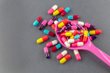 Colorful medicine capsules with spoon isolated on grey background.