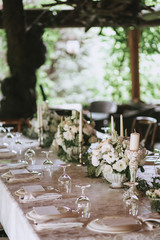 Decorated elegant wedding table for dinner with floral white bouquets, candlesticks and a white tablecloth glasses and porcelain plates