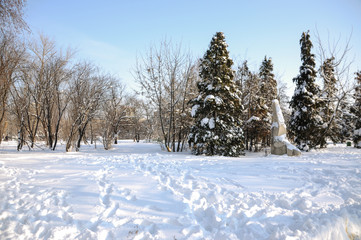 Snow-covered trees, stones, fences and benches in the city park