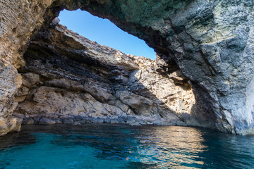 Fototapeta na wymiar Exploring the dramatic huge cliffs and sea caves of south coast of Comino, from sea level on the deep azure crystal clear waters of the Mediterranean, Comino, Malta, June 2017