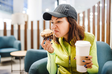 A woman in a fast food cafe with muffin and coffee in her hands smelling spoiled food
