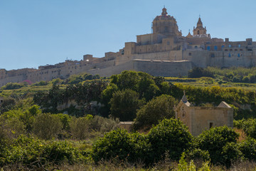 Ancient hilltop fortified capital city of Malta, The Silent City, Mdina or L-Imdina, it's skyline against blue Spring skies with huge walls, domes and towers, over fields of spring flowers, March 2017