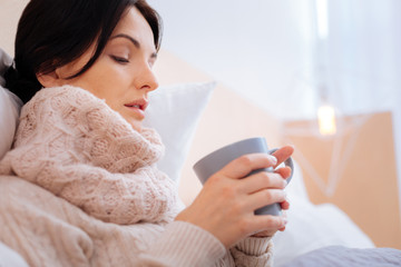 Ill woman looking unhappy while drinking tea