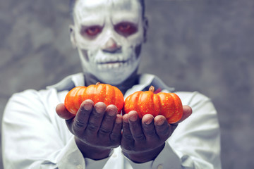 Hands closeup. Human skeleton holding two pumpkins in his hands. The character at Halloween. Man...