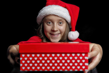 Merry Christmas. A young girl in a red sweater and a Santa Claus hat holds a present - a box