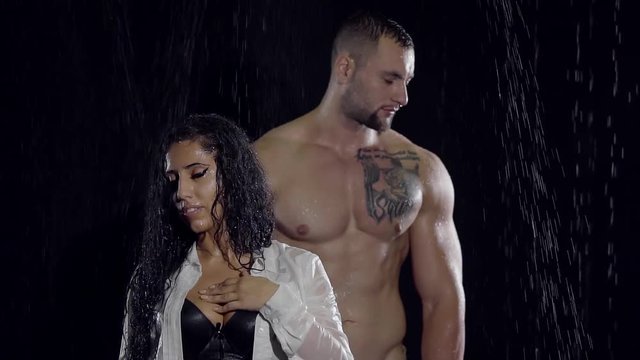 wet naked muscular man is looking to a side and miniature woman is touching her bust, under rain