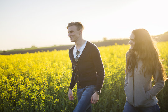Young man and woman walking in canola field at sunset
