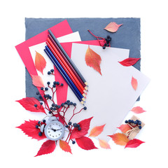 Fototapeta premium Autumn background with an alarm clock, pencils, sheets of paper and autumn leaves. Top view. Space for your text.