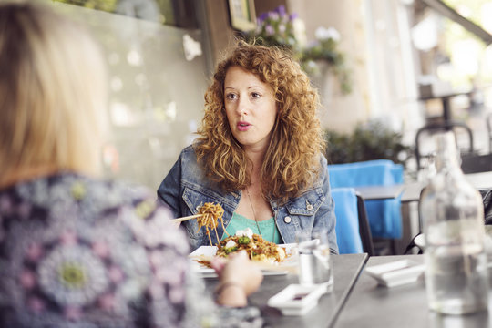 Woman eating pasta while sitting at table with friend