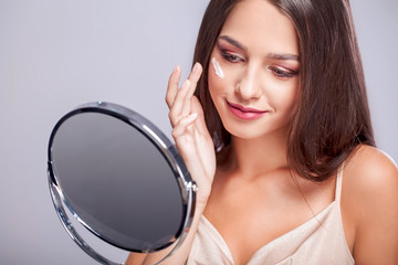 Beauty Face. Closeup Of Sexy Young Woman With Concealer Brush And Mirror In Hands. Portrait Of Beautiful Healthy Female Model Applying Concealer Under Eyes. Skin Cosmetics. High Resolution