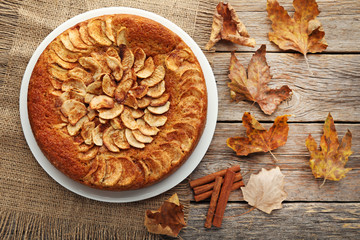 Apple cake with cinnamon and dry leafs on grey wooden table