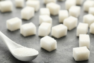 Sugar cubes with white spoon on grey wooden table