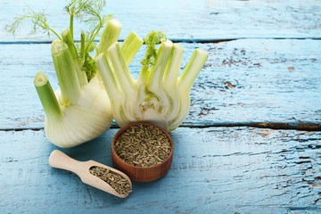 Ripe fennel bulbs and dry seeds in bowl and scoop on blue wooden table