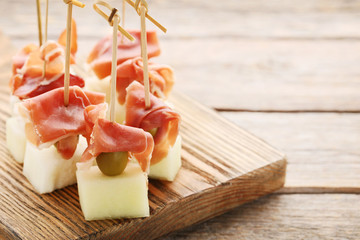 Slices of melon with jamon and olive on skewer on wooden table
