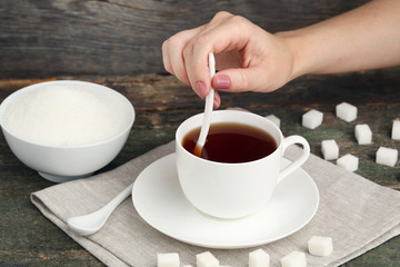 Female hand holding ceramic spoon and cup of tea on wooden table