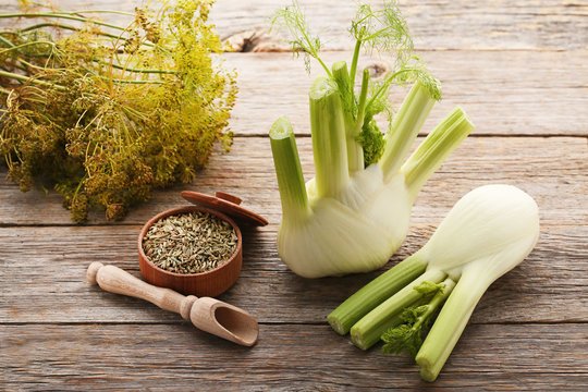 Ripe fennel bulbs and dry seeds in bowl on grey wooden table