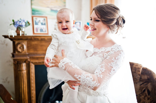 Portrait of a perfect young bride in gorgeous white wedding dress holding a little baby in her hands.