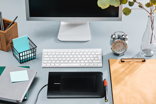 The gray desk with laptop, notepad with blank sheet, pot of flower, stylus and tablet for retouching