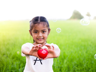 Happy little asian girl holding red heart and smiling.