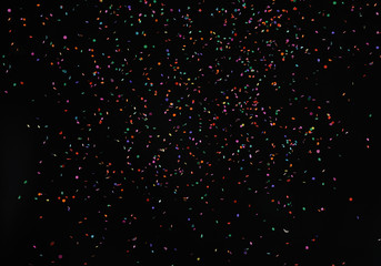 Falling shiny colorful particles confetti glitters texture on black background