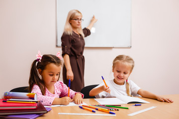 two happy little schoolgirls study in class, the teacher explains